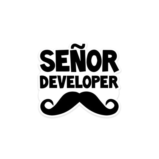 A rectangular sticker with a red background and a white horizontal stripe in the middle. In the center of the white stripe, black Devanagari text reads "घुमक्कड़" which translates to "Wanderer." The red background has faint travel-themed illustrations.