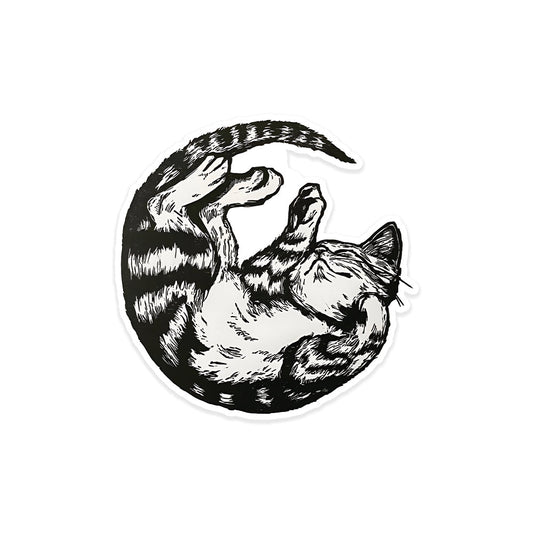 A rectangular sticker with a red background and a white horizontal stripe in the middle. In the center of the white stripe, black Devanagari text reads "घुमक्कड़" which translates to "Wanderer." The red background has faint travel-themed illustrations.